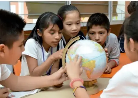 Fotografía de estudiantes de primaria observando un globo terráqueo sobre una mesa, en un salón de clases.