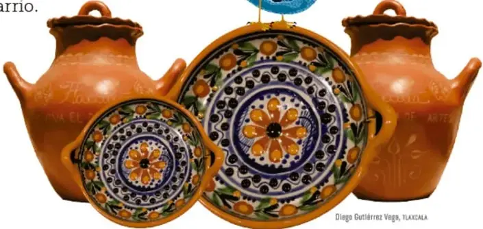 Dos ollas de barro color terracota con asas y dos platos decorados con motivos florales en azul, naranja y verde; sobre el plato central hay un pájaro azul posado. Crédito: Diego Gutiérrez Vega, TLAXCALA.