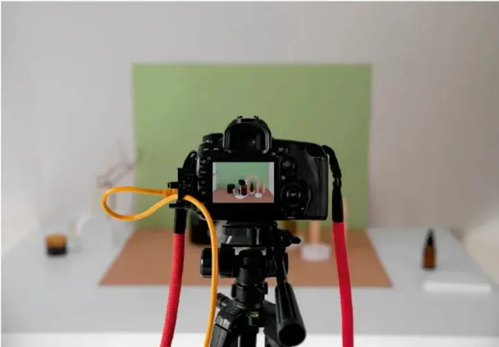 Cámara fotográfica montada sobre un trípode con cables rojo y amarillo, filmando sobre una mesa con artesanías frente a un fondo verde, ilustrando la creación de videos.