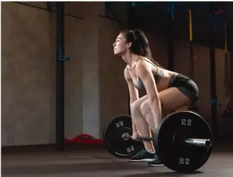 Fotografía de una mujer en un gimnasio levantando una barra con discos de peso (peso muerto), ilustrando la aplicación de fuerza.