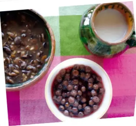 Fotografía de dos tazones con alimentos típicos, uno con frijoles y otro con granos oscuros, sobre un mantel de colores.