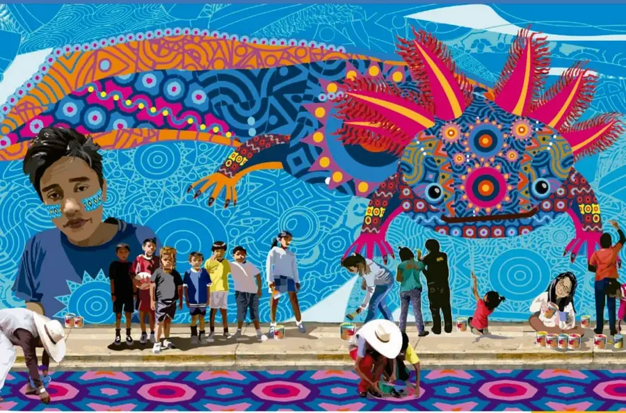Mural ilustrado de un ajolote grande con ornamentos de colores vivos (rosa, naranja, azul y magenta) sobre fondo azul con círculos concéntricos. Una multitud de niñas, niños y adultos con ropa cotidiana y sombreros observa y pinta el mural en la banqueta con cubetas de pintura; a la izquierda destaca el retrato de un niño con pintura en la mejilla.