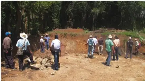 Grupo de personas, algunas con vestimenta tradicional, reunidas en un terreno al aire libre, aparentemente en una actividad comunitaria o asamblea.