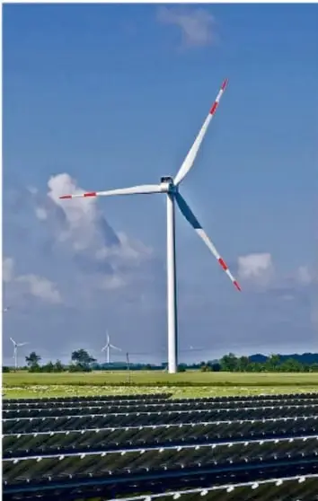 Fotografía de un aerogenerador (molino eólico) sobre un campo con paneles solares en primer plano.