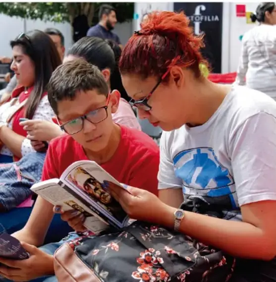 Fotografía de una madre y un niño leyendo juntos un libro en un espacio público.