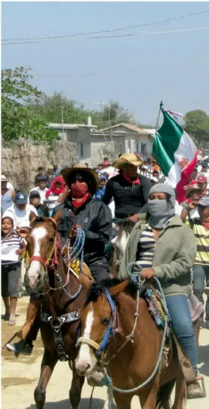Fotografía de una marcha: varias personas montadas a caballo, algunas con el rostro cubierto por pañuelos, avanzan por un camino con la bandera de México ondeando entre la multitud.