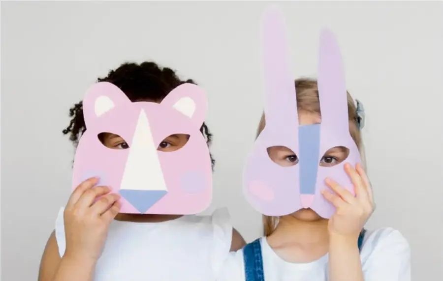 Dos niñas con máscaras de animal: una de oso rosa y otra de conejo lila, sosteniendo las máscaras frente a sus rostros.