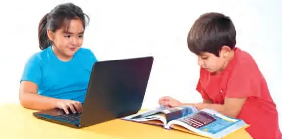 Fotografía de dos niños, Amanda y Benjamín, sentados en una mesa: ella usa un computador portátil y él revisa un libro abierto con mapas, buscando información.