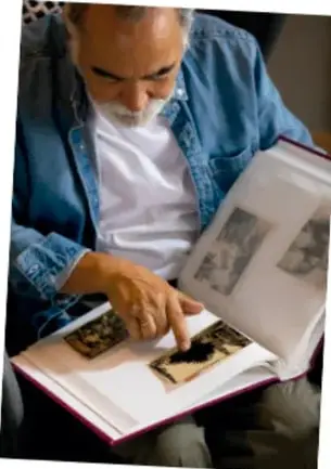 Fotografía de una persona adulta sentada, revisando un álbum de fotografías antiguas; ilustra la solicitud de objetos que muestren cómo era antes la localidad.