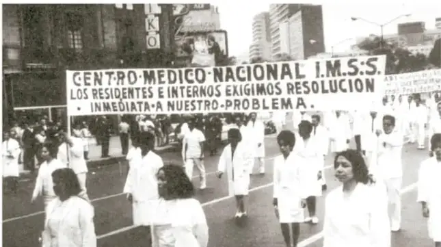 Fotografía en blanco y negro de una marcha de médicos con una pancarta que dice: 'CENTRO MÉDICO NACIONAL I.M.S.S. LOS RESIDENTES E INTERNOS EXIGIMOS RESOLUCIÓN INMEDIATA A NUESTRO PROBLEMA'.