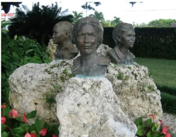 Fotografía a color de bustos escultóricos de las hermanas Mirabal sobre un monumento de roca en un jardín, con flores al frente.