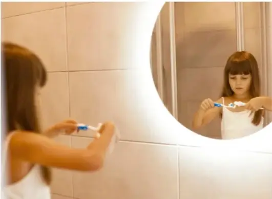 Niña cepillándose los dientes frente al espejo del baño, ejemplo de hábito frecuente.