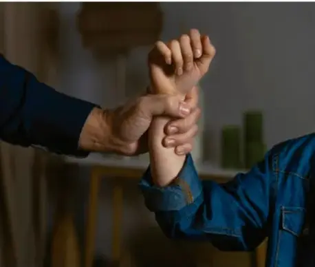 Fotografía de una mano adulta sujetando con fuerza la muñeca de otra persona, ilustrando la coerción propia de la trata de personas.