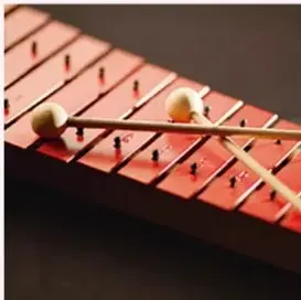 Xilófono de láminas metálicas con dos macillos, ilustrando la producción de sonidos por vibración.