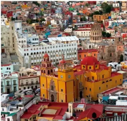 Vista panorámica de una ciudad colonial latinoamericana con edificios coloridos, cúpulas y torres de iglesias (Guanajuato, México), representando la arquitectura heredada del periodo colonial.