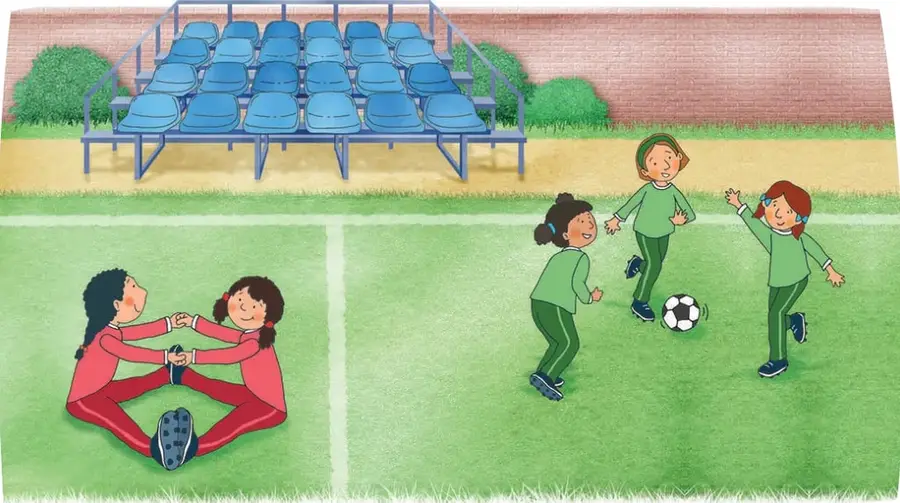 Cancha de fútbol con pasto, arco de fondo, muro de ladrillos y graderías con sillas azules; tres niñas con uniforme verde juegan con un balón.