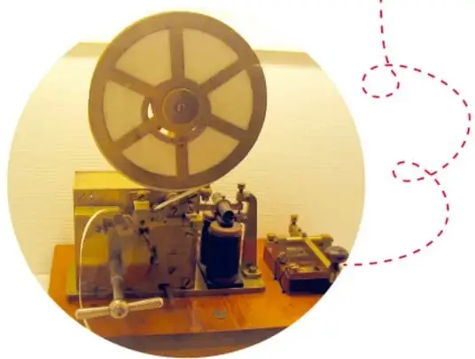 Fotografía de un telégrafo antiguo de madera y metal, con un carrete de cinta de papel circular en la parte superior y una llave telegráfica con palanca.