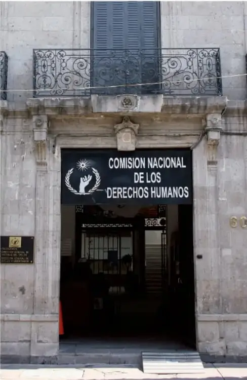 Fotografía de la fachada del edificio de la Comisión Nacional de los Derechos Humanos, con un letrero que dice 'COMISIÓN NACIONAL DE LOS DERECHOS HUMANOS' y una placa conmemorativa.