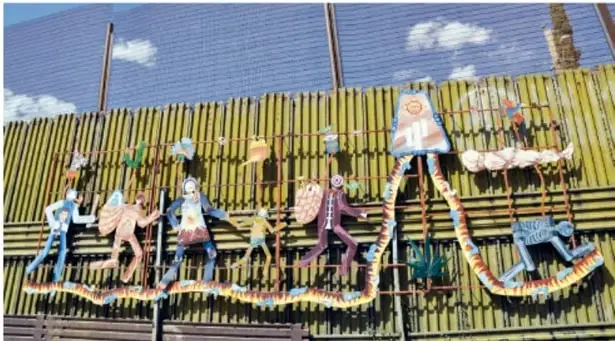 Mural de figuras humanas estilizadas que corren o bailan pintado sobre una barda de lámina o varillas verdes.
