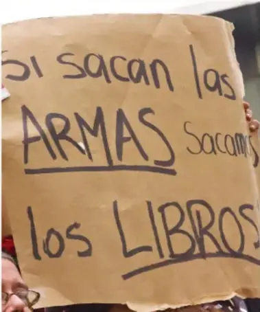 Fotografía de una persona sosteniendo un cartel de cartón con la frase 'Si sacan las ARMAS sacamos los LIBROS'.