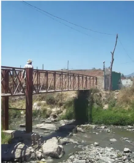 Fotografía de un puente de madera sobre un río con vegetación y un paisaje rural, que ilustra la relación entre las personas y el entorno natural.