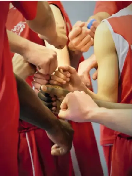 Fotografía de manos de jóvenes juntándose al centro como gesto de unión, con uniformes deportivos rojos.