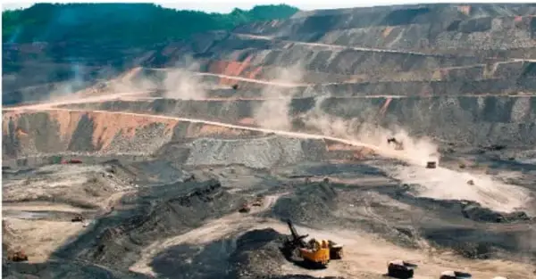 Fotografía de una mina a cielo abierto: un enorme tajo con bancos escalonados, maquinaria amarilla y polvo de la extracción.