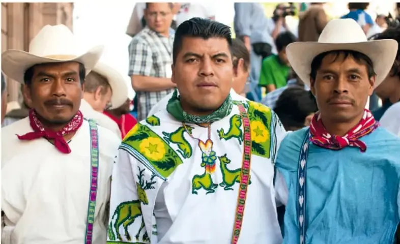 Fotografía de tres hombres con sombreros de ala ancha, camisas bordadas y paliacates, posando en un evento público; ilustra la diversidad cultural del norte de México.