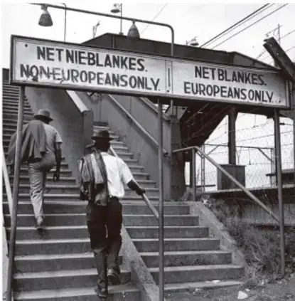 Fotografía en blanco y negro de una escalera con letreros que dicen 'NET NIEBLANKES. NONEUROPEANS ONLY' y 'NET BLANKES. EUROPEANS ONLY', mostrando la segregación racial en espacios públicos.