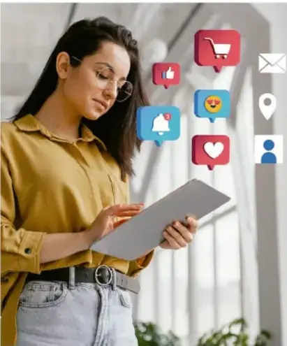 Mujer joven de cabello largo y lentes, con blusa mostaza, sostiene una tableta electrónica; a su alrededor flotan íconos de redes sociales: carrito de compras, 'me gusta', carita sonriente, corazón, ubicación y perfil de usuario.