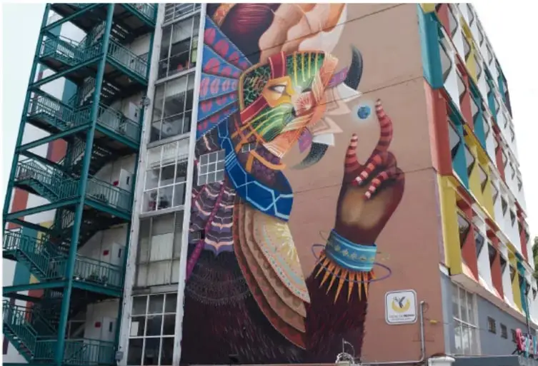 Fotografía de un mural de gran formato pintado en la fachada de un edificio público, con una figura humana y colores vivos.