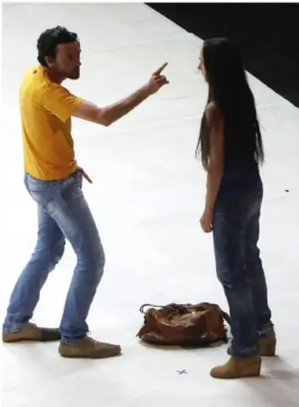 Fotografía de un hombre gritando y señalando a una mujer, con una bolsa en el suelo, representando violencia verbal.