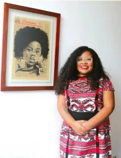 Fotografía de una mujer afro-mexicana sonriente frente a un retrato enmarcado; crédito: Max Jowan Longo Resendiz, Estado de México.
