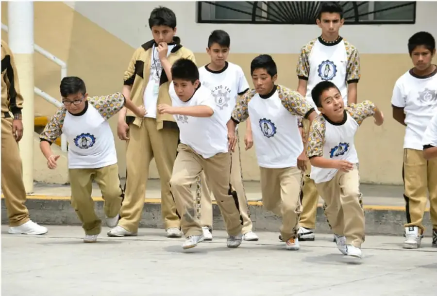 Fotografía de un grupo de adolescentes estudiantes de Telesecundaria, con uniforme blanco y pantalón khaki, corriendo en el patio de su escuela durante una actividad física.