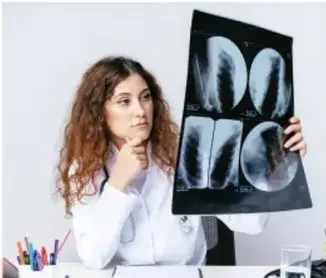 Fotografía de una médica sosteniendo una radiografía de tórax frente a una fuente de luz.