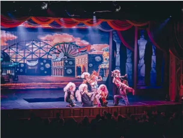 Fotografía de una obra teatral con varios actores en trajes de época (tapando los ojos con la mano), escena de carácter cómico o de enredo.