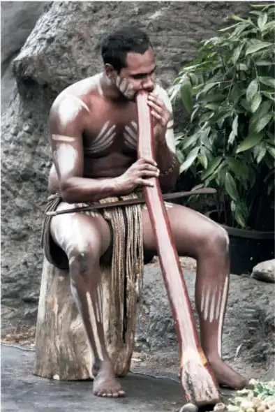 Hombre aborigen australiano con pinturas blancas en el cuerpo tocando un didgeridoo.