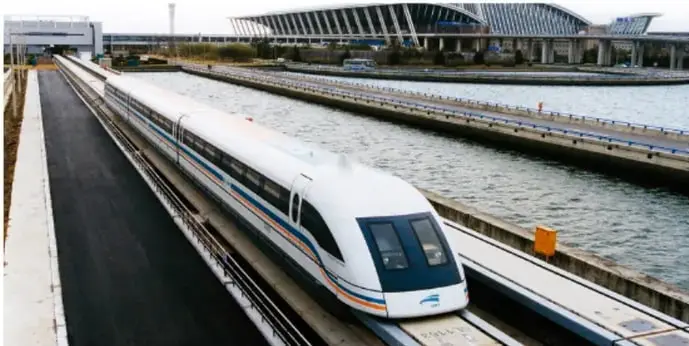 Tren de levitación magnética (maglev) desplazándose sobre una vía elevada junto al agua, con una estación al fondo.
