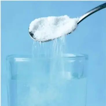 Cuchara con azúcar blanca disolviéndose en un vaso con agua, ilustrando la solubilidad.
