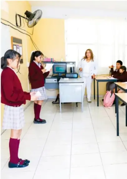 Estudiantes de telesecundaria presentan su proyecto con ayuda de una computadora frente a su maestra y compañeros en el aula.