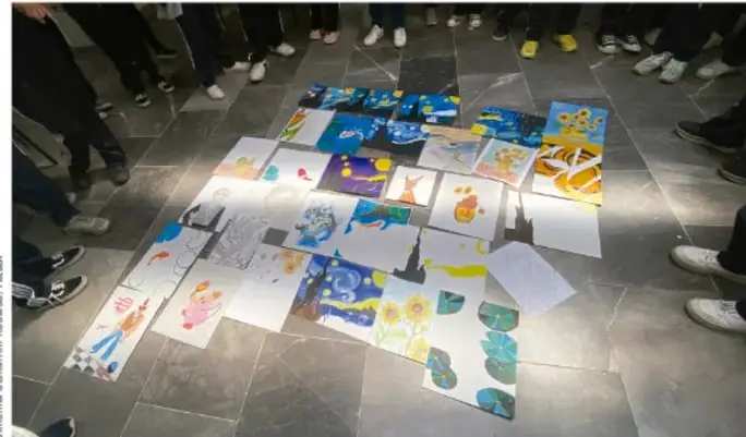 Fotografía del mural escolar desplegado en el piso, rodeado de estudiantes, con dibujos y textos en papelitos de colores.