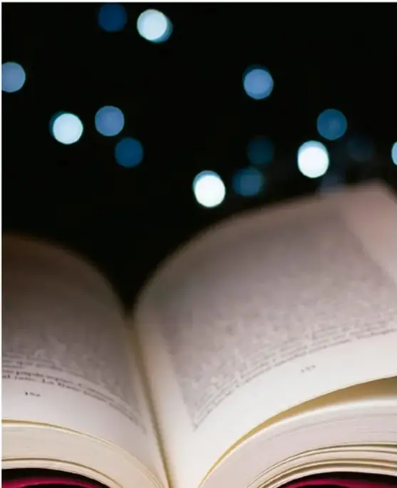 Fotografía de un libro abierto con páginas iluminadas sobre un fondo oscuro con luces desenfocadas (bokeh) azules y blancas, evocando la lectura y la reflexión.