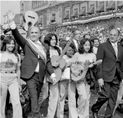 Fotografía en blanco y negro de José López Portillo saludando en un acto público, acompañado de personas.