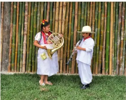 Dos personas con instrumentos musicales (corno francés y clarinete) frente a una pared de bambú.