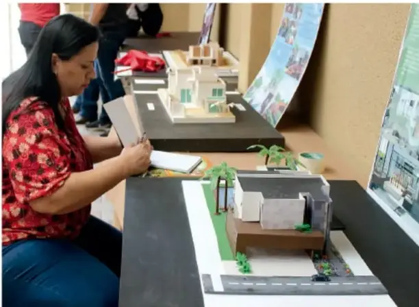 Una persona coloca una maqueta sobre una mesa; se observan calles, casas y áreas verdes.