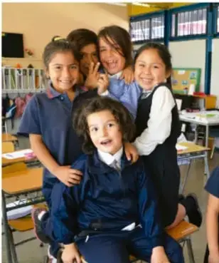 Fotografía de un grupo de estudiantes de primaria sonriendo dentro del salón de clases, sentados en sus pupitres.
