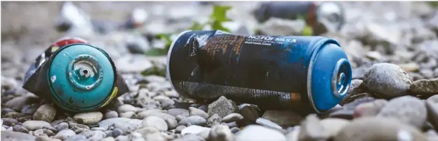 Fotografía de latas y residuos sólidos abandonados sobre un lecho de piedras, representando la contaminación que degrada el suelo.