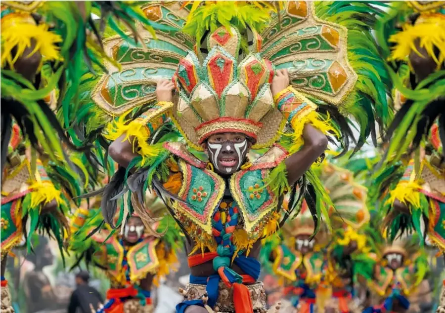 Fotografía de un bailarín de carnaval con un gran tocado verde, amarillo y rojo, en pleno desfile.