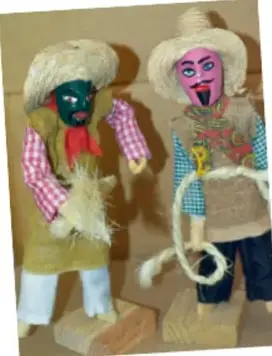 Dos figuras disfrazadas con vestuario tradicional: sombrero de paja, máscara verde y rosa, ropa de colores, posiblemente muñecos o danzantes típicos.