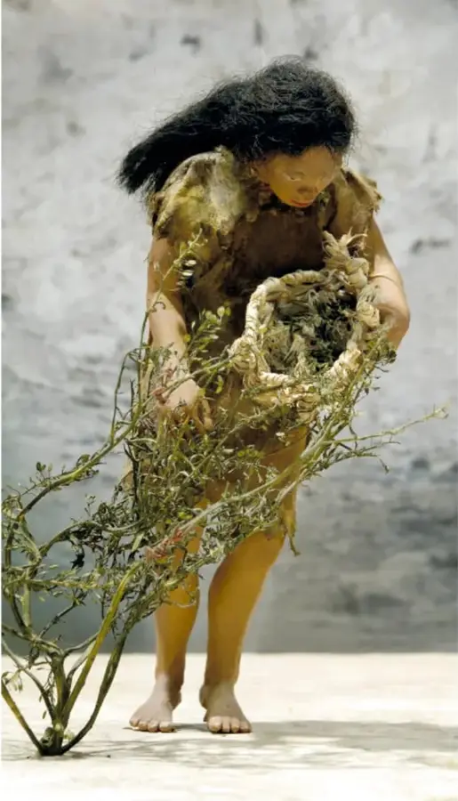 Maqueta en paisaje nevado: personas de la prehistoria deshuesando y secando carne colgada en un armazón de palos.